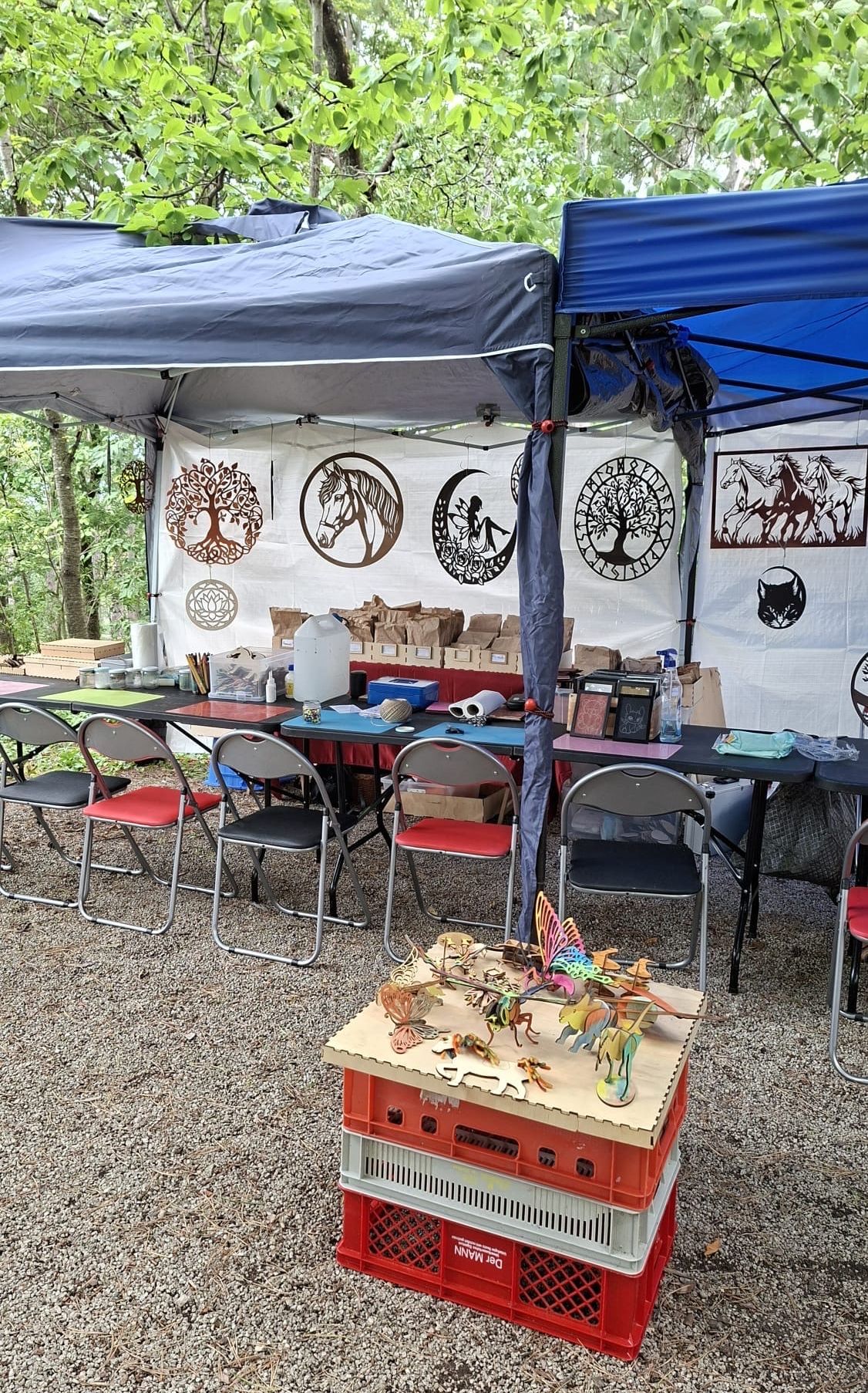 Ein Zelt mit verschiedenen ausgestellten Gegenständen darunter, einschließlich Kunstwerke, ein Tisch mit Objekten und Stühlen. Verschiedene Kisten und Taschen sind ebenfalls vorhanden. Das Zelt ist mit hängenden Dekorationen geschmückt.