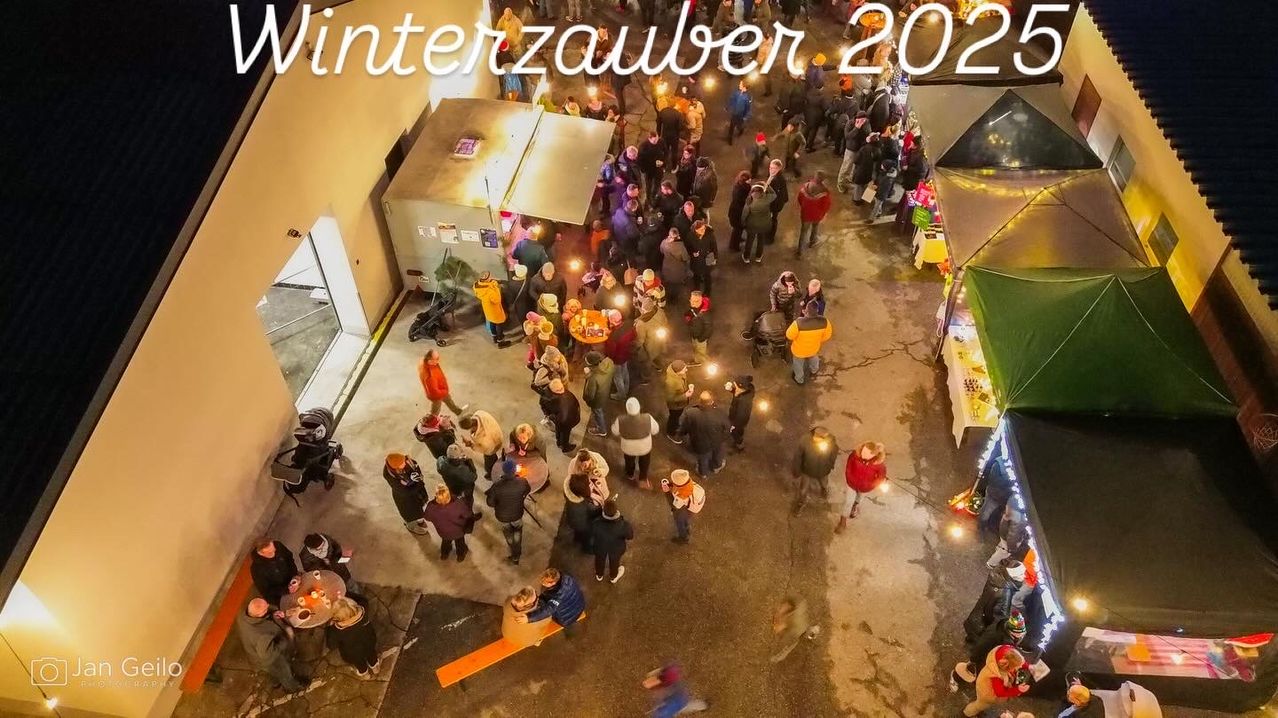 An aerial view of a crowded street during winter with people holding candles. A large banner above reads 'Winterzauber 2022.'