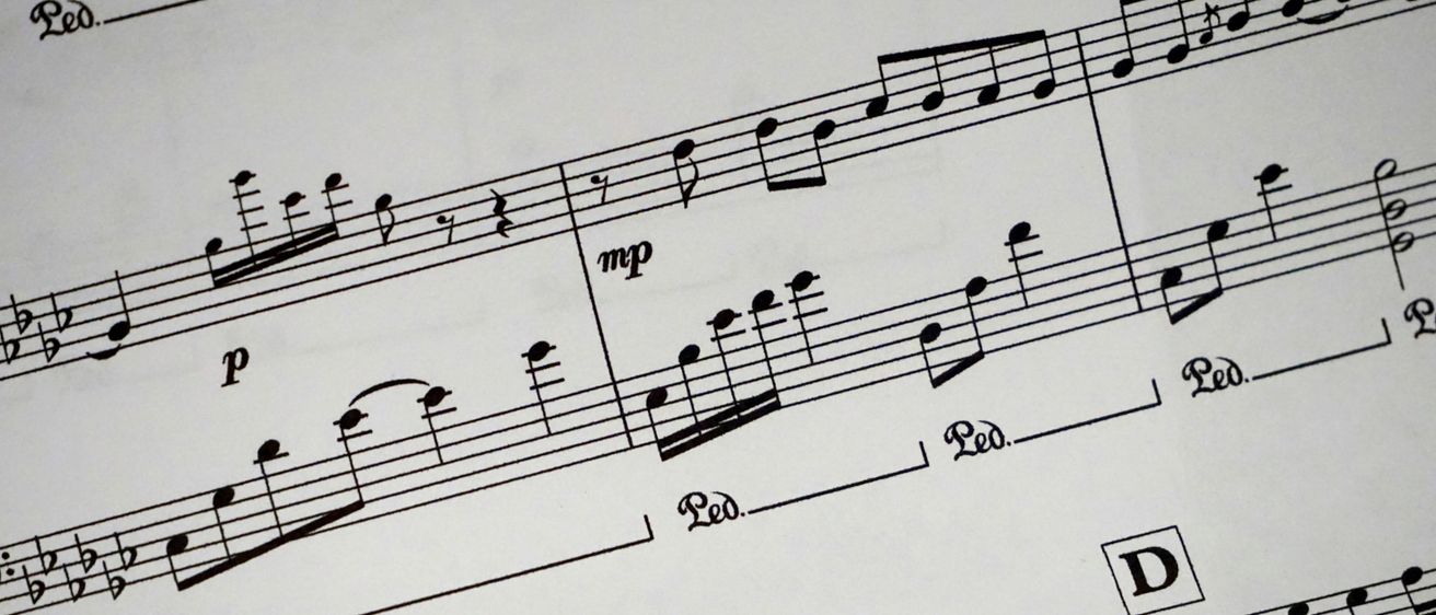 Eine Nahaufnahme eines Notenblattes mit Musiknoten, Takten und Tempobezeichnungen. Auf dem Blatt stehen die Texte 'mp' und 'Ped.'. Das Blatt ist weiß mit schwarzer Tinte.