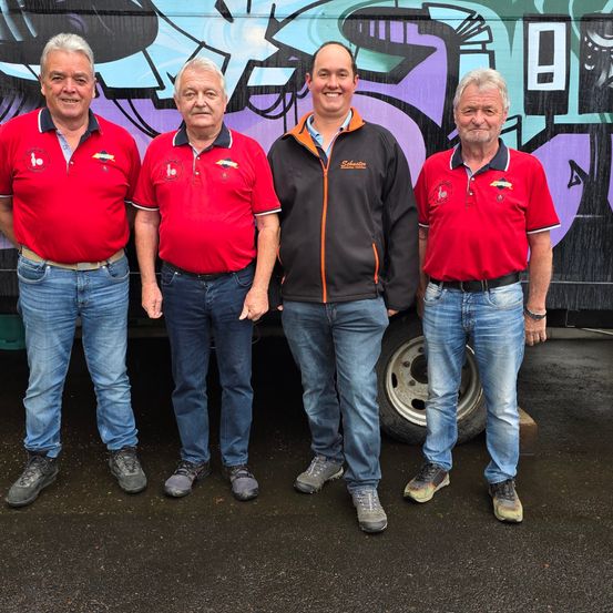 Vier Männer in roten Poloshirts und Jeans stehen vor einer mit Graffiti bedeckten Wand.