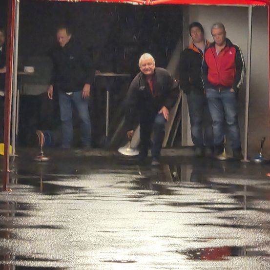 Eine Gruppe von Männern steht in einem nassen Bereich, möglicherweise bei einem Wettbewerb. Ein Mann lächelt und hält eine Scheibe.