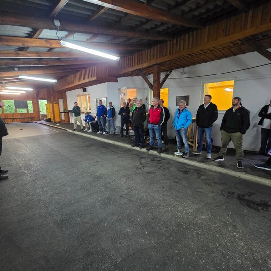 Eine Gruppe von Menschen steht an der Seite einer Indoor-Einrichtung und trägt Winterkleidung. Sie warten wahrscheinlich darauf, dass etwas passiert.