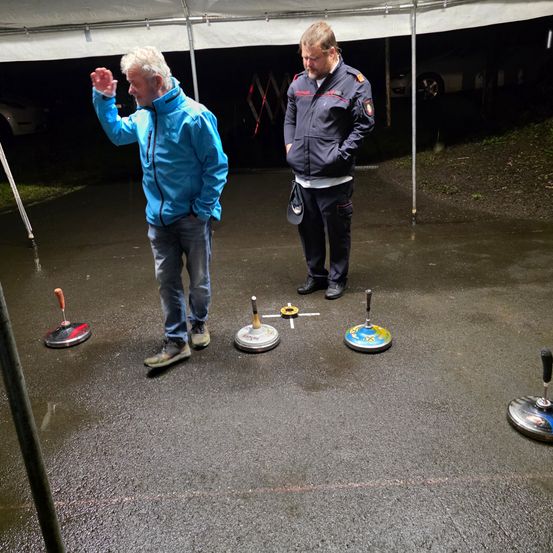 Zwei Männer stehen unter einem Zelt und unterhalten sich, während sie auf einen Boden mit kreisförmigen Objekten schauen, die wie Scheiben aussehen.