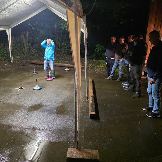 Eine Gruppe von Männern spielt im Dunkeln im Freien unter einem Zelt eine Partie Shuffleboard.