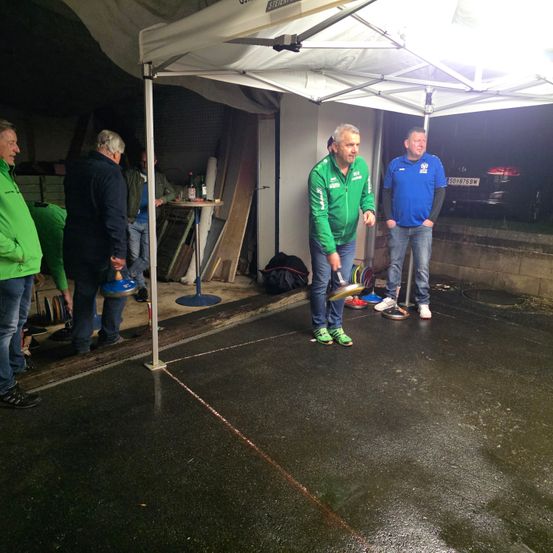 Mehrere Männer stehen nachts in einem Zelt. Ein Mann hält eine Frisbee, während ein anderer Mann eine grüne Jacke trägt.