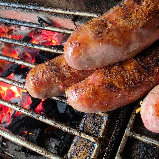 Nahaufnahme von mehreren Würsten, die auf einem Grillrost mit roter Flamme darunter garen.