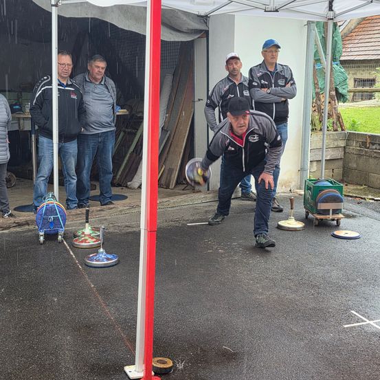 Fünf Männer in einer Garage mit offener Tür spielen ein Spiel mit einem Ball und einem Ziel.