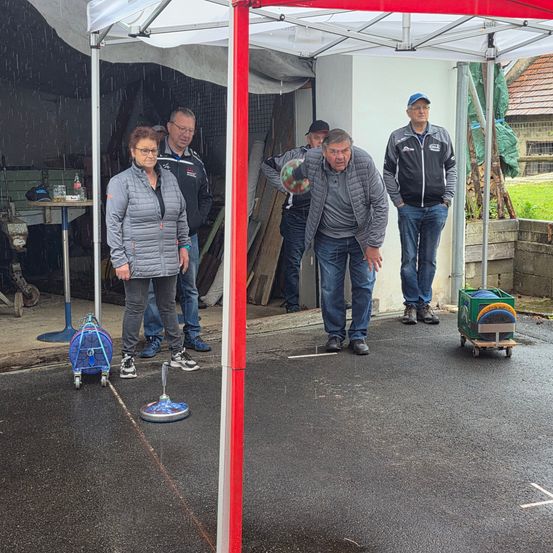 Eine Gruppe von Menschen in einem Schutz während des Regens, zwei Männer werfen eine Frisbee.