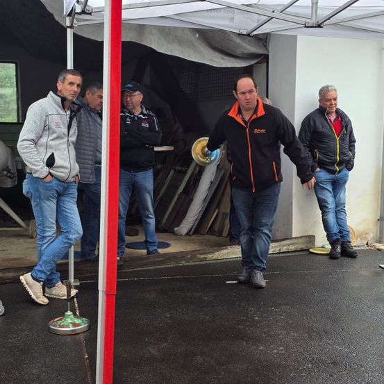 Vier Männer stehen unter einem Zelt, zwei von ihnen stehen mit den Händen in den Taschen. Die anderen beiden Männer gehen, einer von ihnen hat eine Scheibe in der Hand.