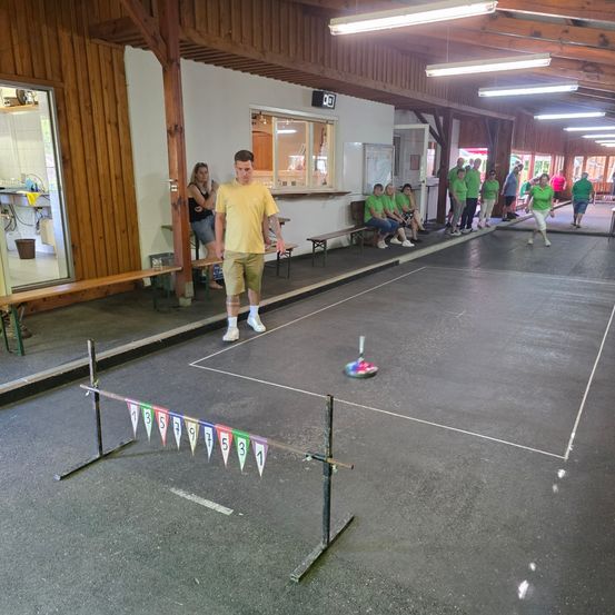 Eine Gruppe von Menschen in grünen Uniformen spielt Tischtennis in einer Halle. Ein Mann steht in der Nähe des Tisches, und andere schauen zu.