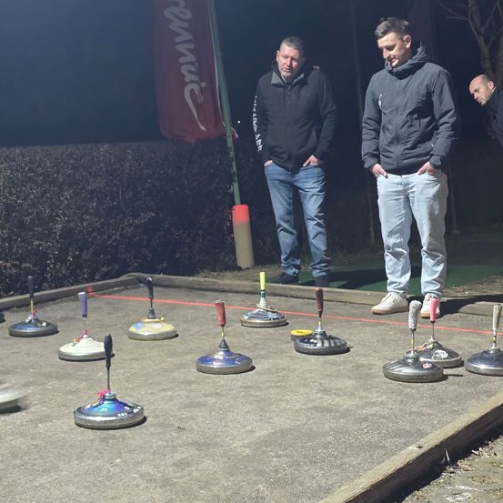 Drei Männer stehen bei einem Bocce-Ballplatz in der Nacht, einer der Männer schaut in die Kamera.