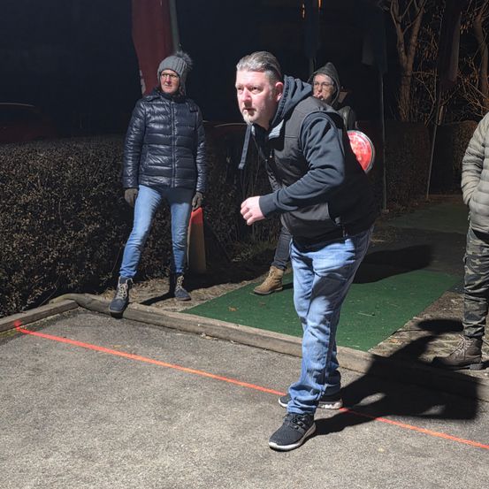 Ein Mann in einer Kapuzenjacke bereitet sich darauf vor, nachts einen Frisbee zu werfen. Zwei Personen stehen hinter ihm und eine weitere beobachtet von der Seite.