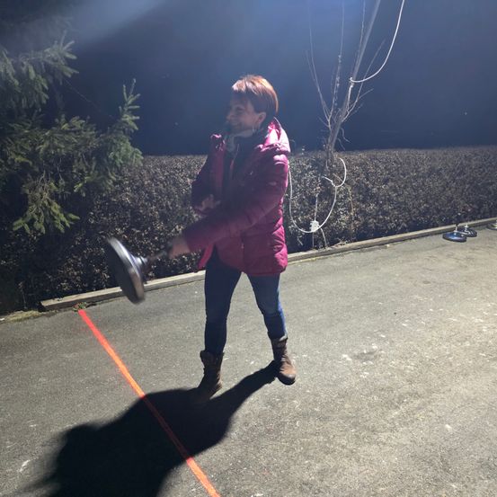 Eine Frau in einer rosa Jacke und braunen Stiefeln wirft eine Scheibe in einem Parkplatz bei Nacht.