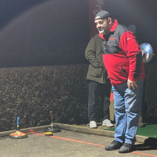 Zwei Männer stehen in der Nähe einer Wand mit zwei kleinen Objekten. Ein Mann schaut auf die Objekte, während der andere Mann zuschaut. Die Szene ist schwach beleuchtet.