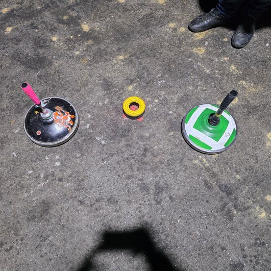 Drei verschiedene Yo-Yos liegen auf dem Betonboden. Eines hat einen rosa Griff, eines ist gelb und das andere grün. Ein Schatten einer Person ist auf dem Boden.