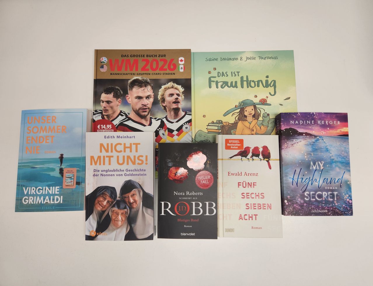A row of books on a white background includes 'Das Grosse Buch Zur WM 2026', 'Nicht Mit Uns!', 'Robb', 'Das Ist Frau Honig', 'Nadine Kern', and 'My Highland Secret'.