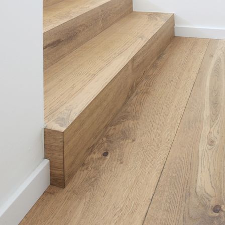 Nahaufnahme von hellen Holzstufen, die zu einer weißen Wand und einem Boden führen.