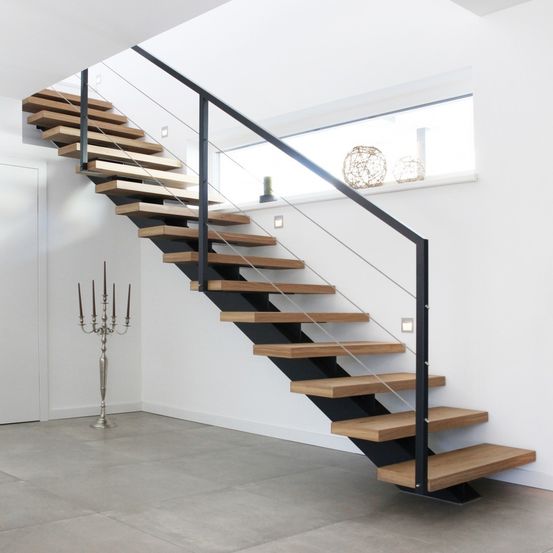 Eine moderne Treppe mit Holzstufen und schwarzen Metallhandläufen. Der Raum ist hell mit weißen Wänden und einem Fenster mit Blick auf eine Pflanze.