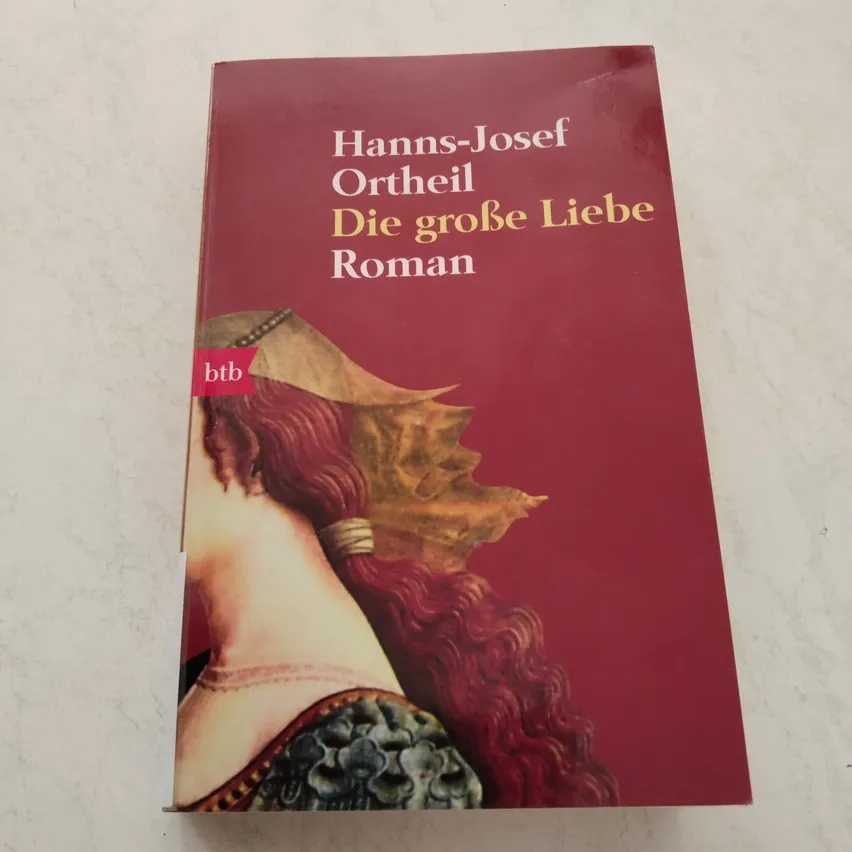 Ein Buchcover mit rotem Hintergrund, das eine Frau mit langen, lockigen roten Haaren und einem goldenen Kopfschmuck zeigt. Der Titel lautet 'Die große Liebe' von Hanns-Josef Ortheil.