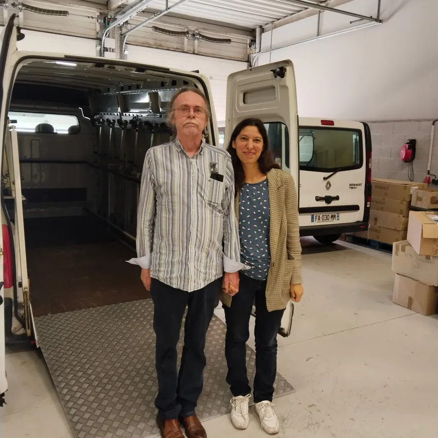 Ein Mann und eine Frau stehen in einem Lagerhaus. Der Mann trägt ein gestreiftes Hemd und braune Schuhe. Die Frau trägt ein blaues Hemd und weiße Schuhe.