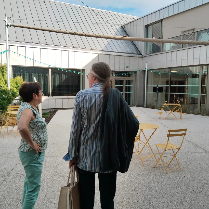 Zwei Personen stehen vor einem modernen Gebäude. Der Mann hält eine Tasche, und die Frau schaut ihn an.