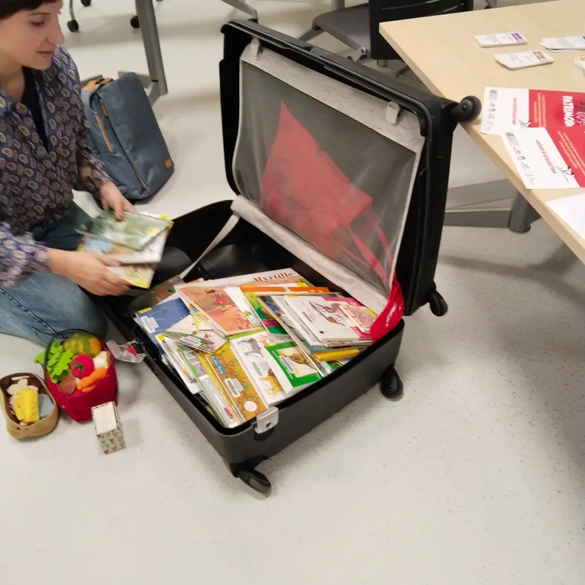 Eine Frau sitzt auf dem Boden und packt einen Koffer voller Bücher und Spielzeug aus.