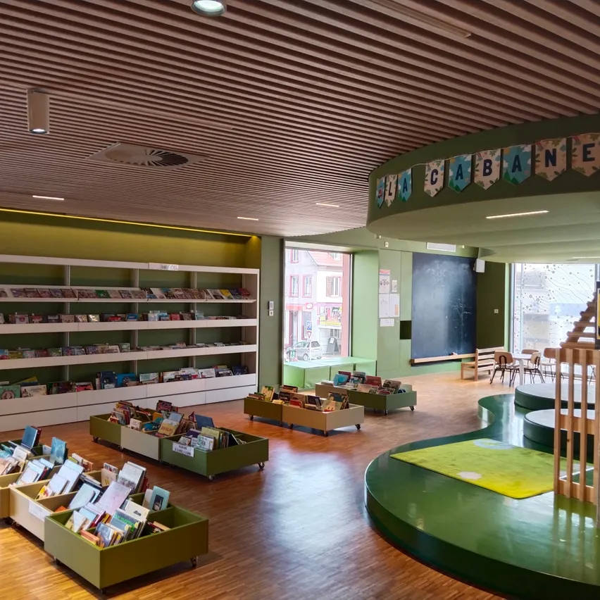 Eine Innenbibliothek mit Holzböden und Regalen voller Bücher. Es gibt auch Tische und Stühle zum Lesen.