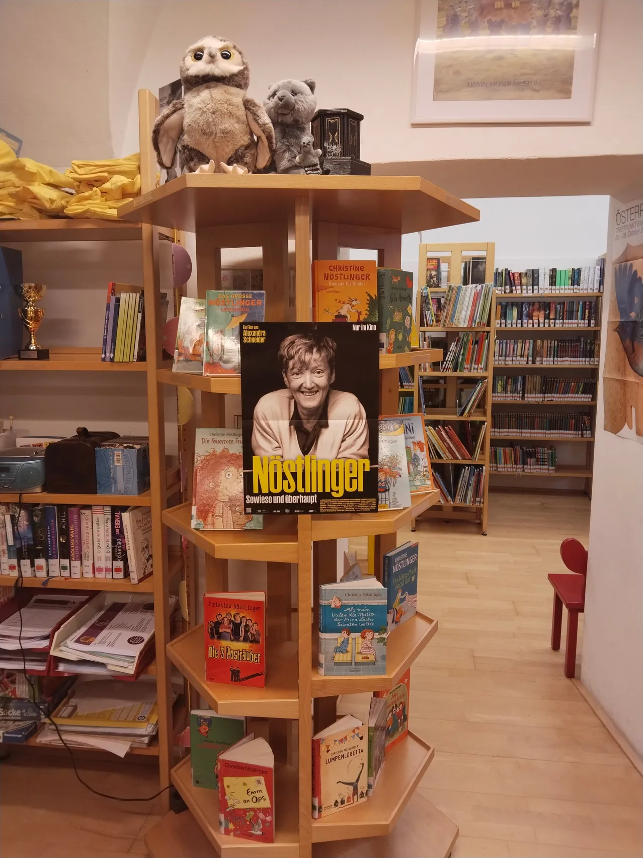 Eine Bibliothek mit einem Bücherregal voller Bücher und einem Plakat einer Frau obenauf.