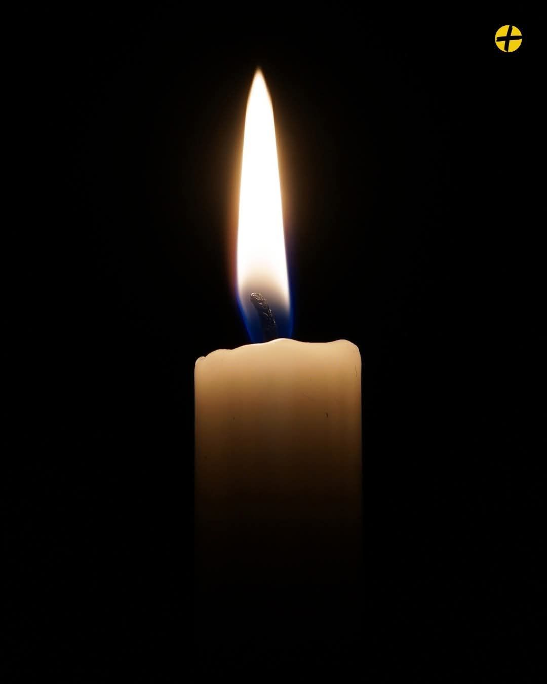 Eine einzelne Kerze ist im Dunkeln angezündet. Die Flamme ist hell und flackert sanft. Die Kerze ist weiß und scheint in einem Kerzenhalter zu brennen.