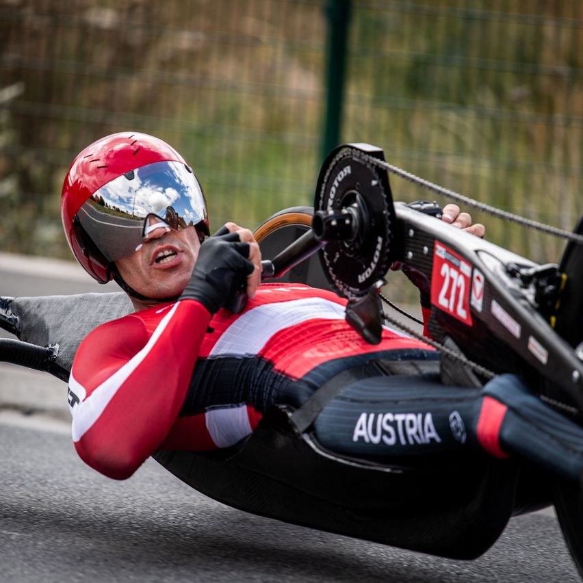 Ein Athlet in rot-weißer Kleidung, mit Helm, fährt auf einer Rennstrecke mit der Nummer 272 am Fahrrad.