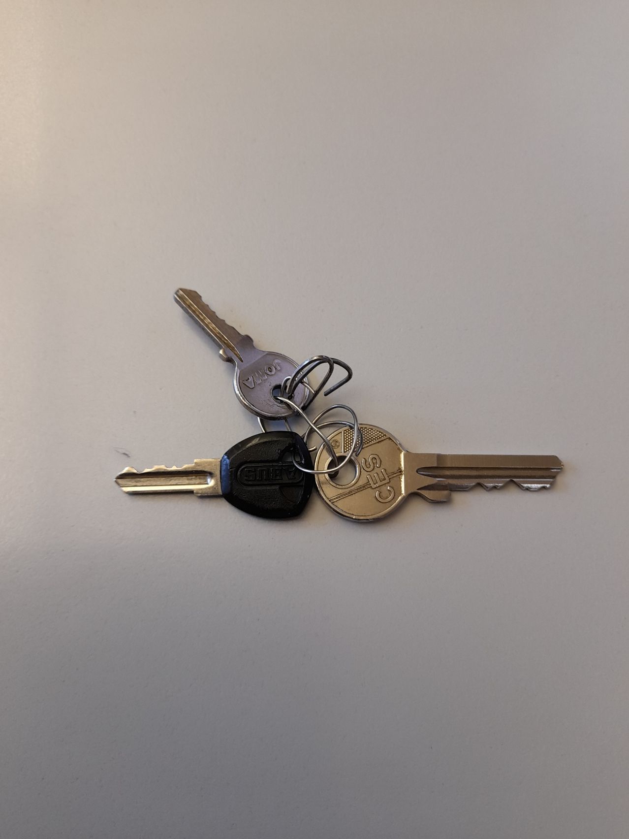 Drei Schlüssel auf einer weißen Oberfläche. Der obere Schlüssel ist silber mit einem silbernen Ring, der mittlere Schlüssel ist schwarz und der untere Schlüssel ist silber mit einem Logo.