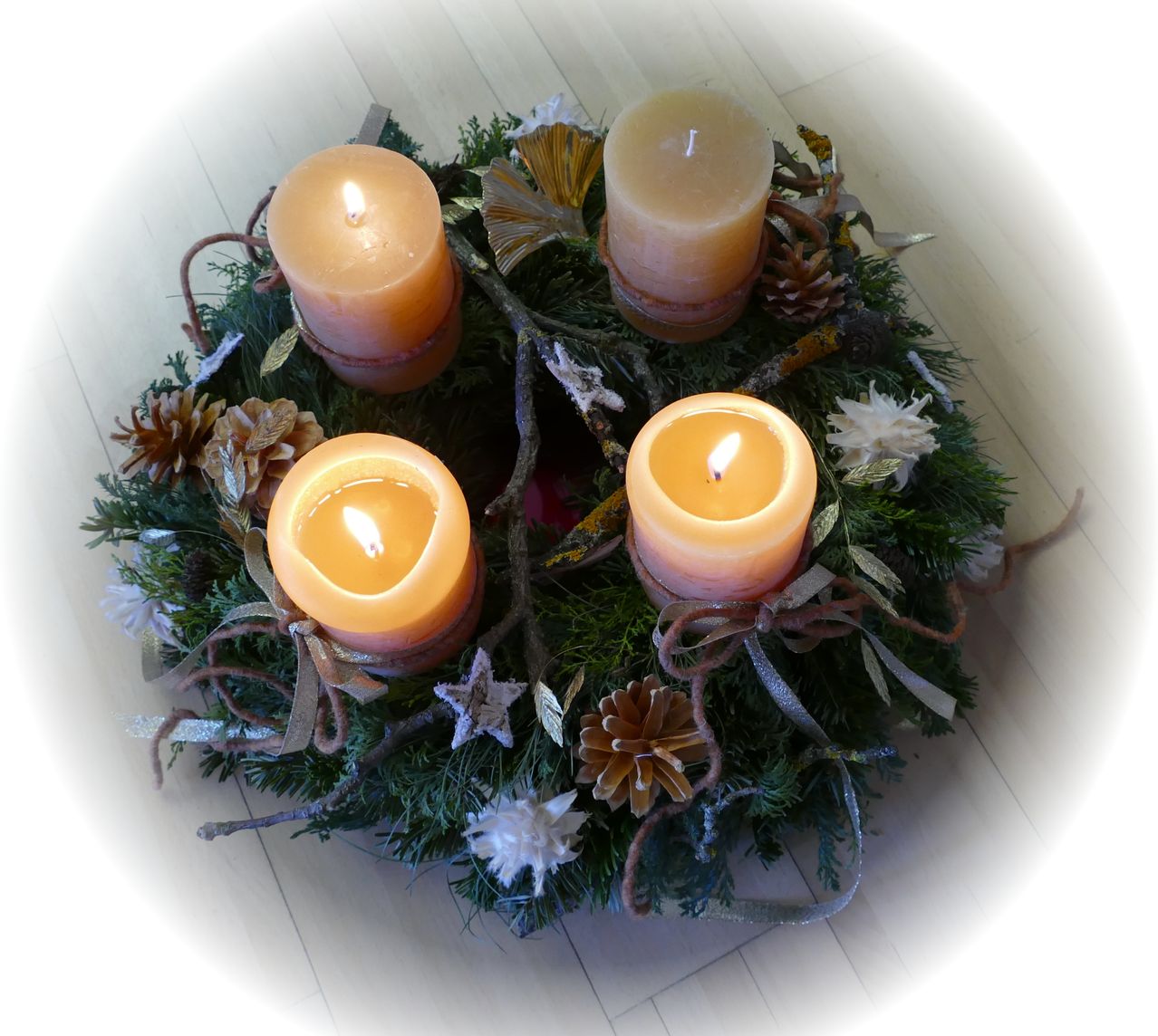 Ein Kranz mit vier brennenden Kerzen, Tannenzapfen und Grün auf einer Holzoberfläche.