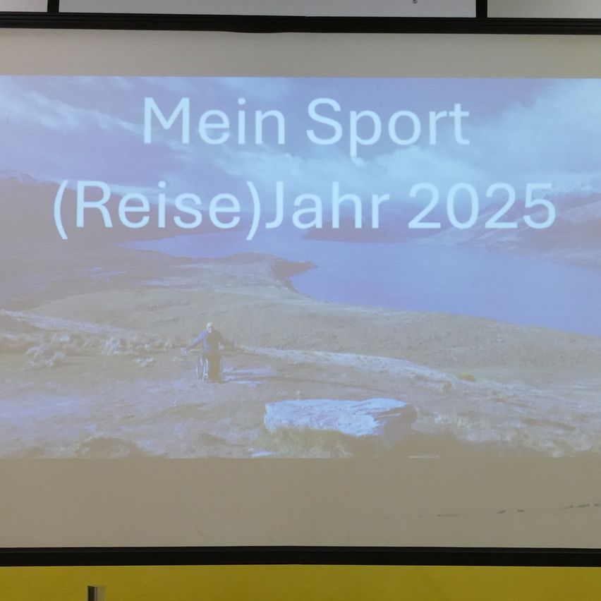 Ein projiziertes Bild zeigt einen Mann im Rollstuhl in einer landschaftlichen Umgebung. Über dem Bild stehen die Worte 'Mein Sport (Reise)Jahr 2025'.