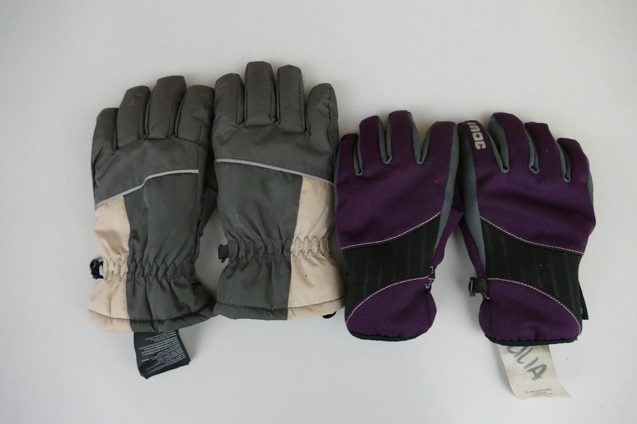 Drei Paar Handschuhe sind zu sehen: ein Paar ist schwarz und beige, ein weiteres Paar ist lila und schwarz und das dritte Paar ist lila und grau. Alle Handschuhe haben ein Etikett auf der linken Seite.