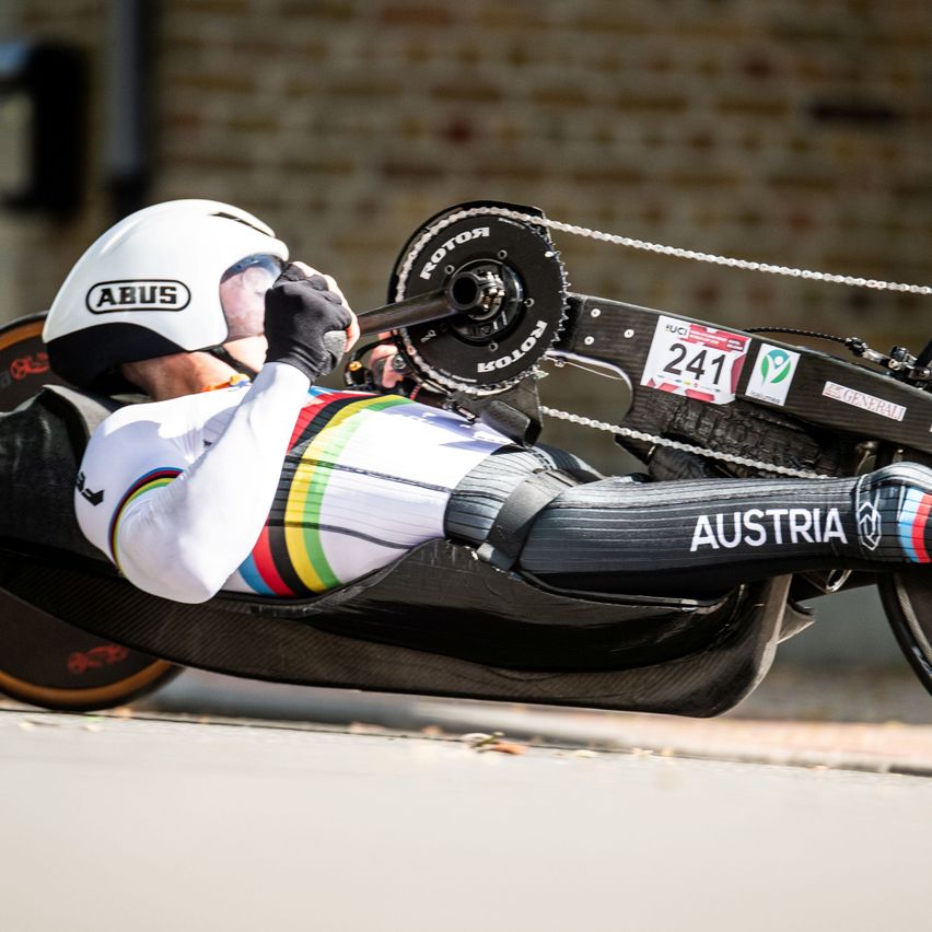 A cyclist wearing an ABUS helmet leans forward on a carbon bike with Austria on the side. He holds the handlebars with one hand and wears gloves.