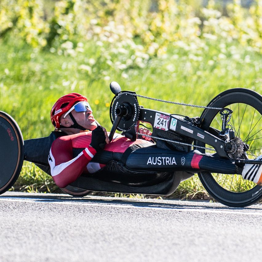 A male cyclist in a red helmet and glasses, wearing a red and white suit, rides a bike with the number 241 on a road. The bike is lying on its side.