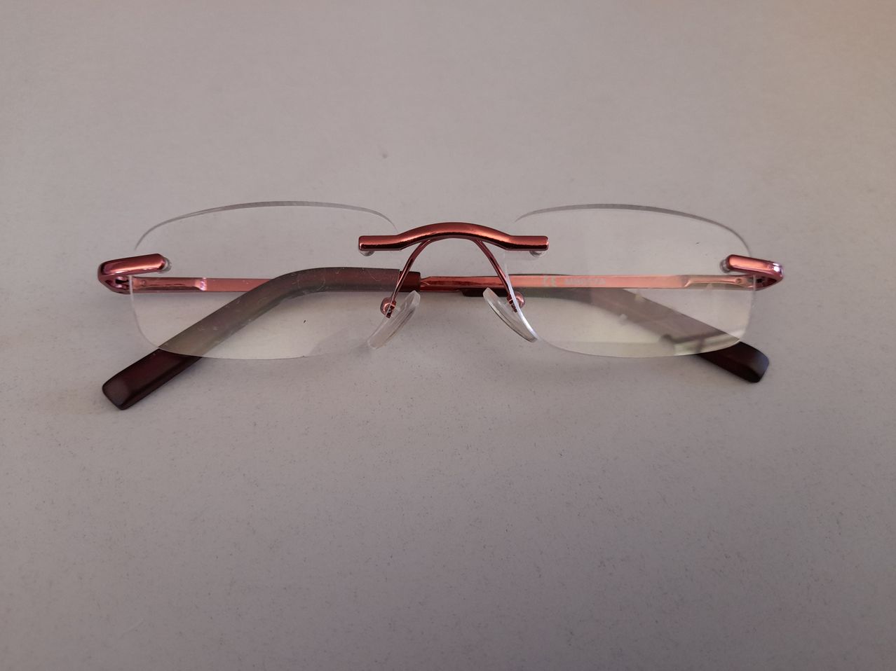 Ein Paar Brille mit rosegoldfarbenen Rahmen und klaren Gläsern liegt auf einer weißen Oberfläche.