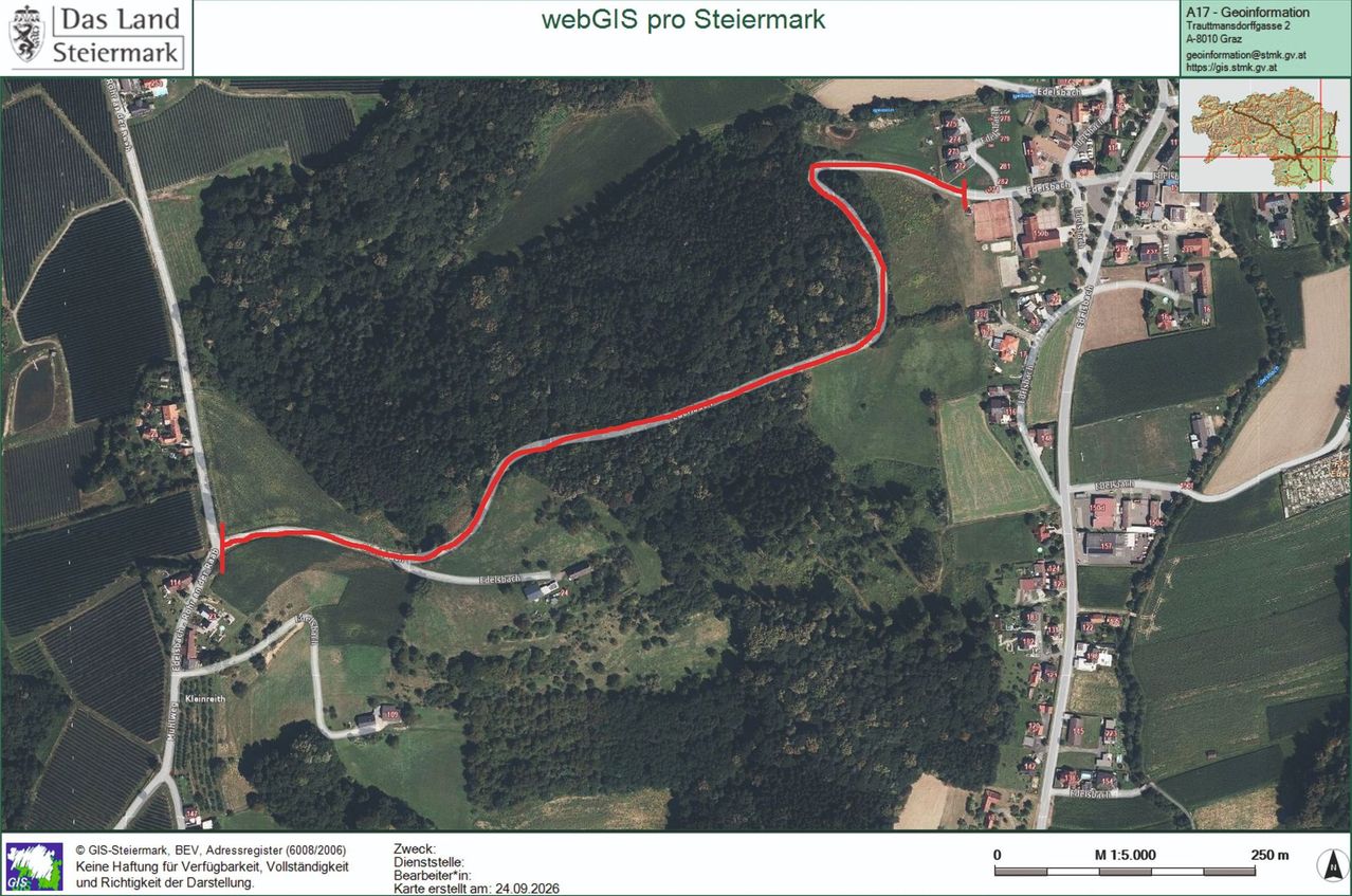 Luftaufnahme eines ländlichen Gebiets mit einer sich windenden roten Linie, die einen Weg oder eine Straße anzeigt. Das Gebiet ist von Grün umgeben, und es sind Gebäude und Häuser sichtbar. Das Bild enthält einen Maßstab und einen Datumsstempel.