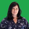 Eine Frau mit schwarzen Haaren und einem Blumenbluse steht vor einem grünen Hintergrund und lächelt freundlich in die Kamera.