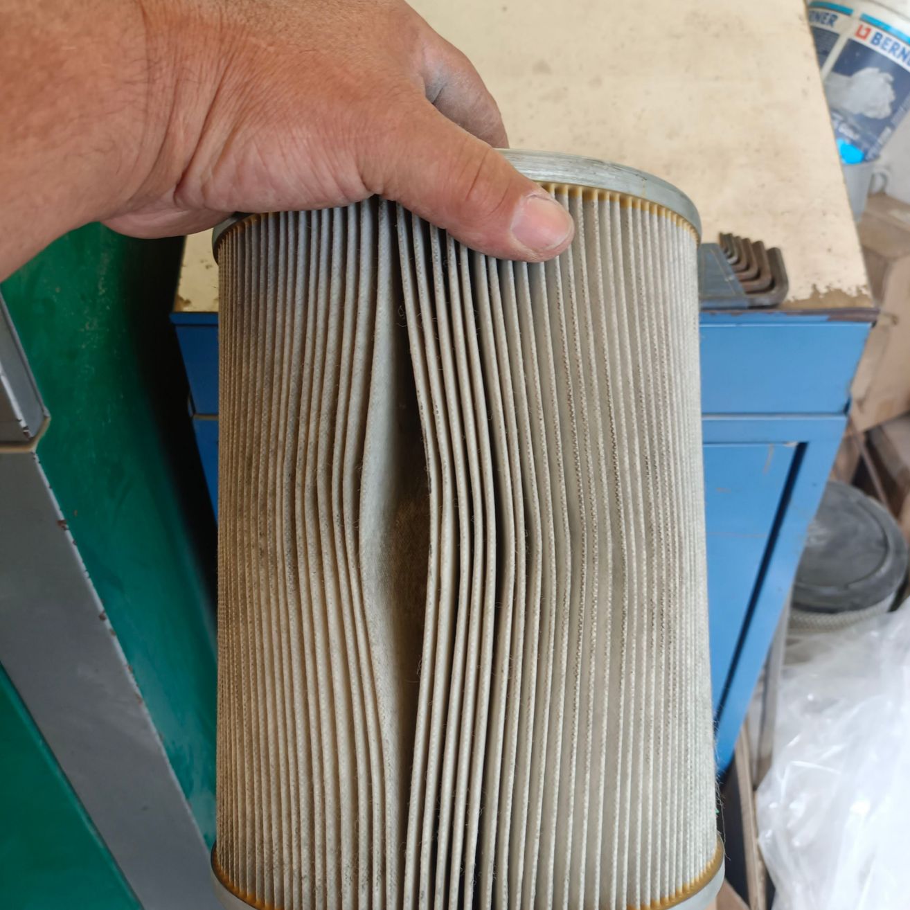 Eine Person hält einen alten zylindrischen Luftfilter mit einem Metallring oben und einem gefalteten Papierfilter im Inneren.