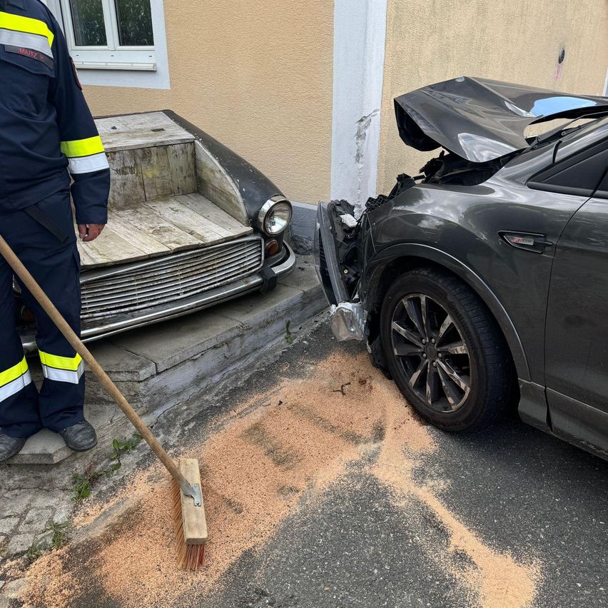 Eine Person in Uniform fegt einen Getreideverschüttung in der Nähe eines verunglückten Autos gegen ein Gebäude.