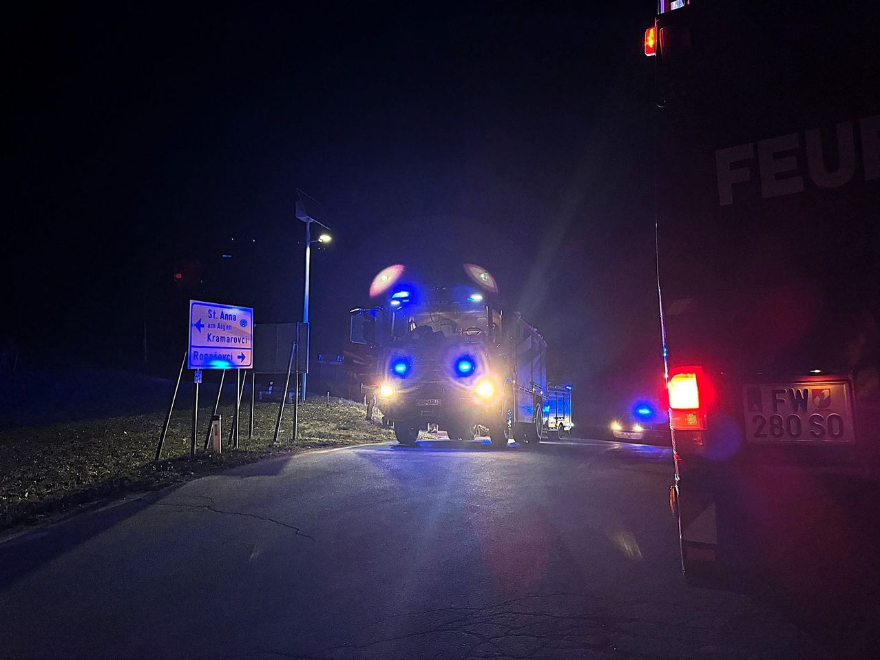 Ein Feuerwehrwagen mit blauen Blinklichtern fährt bei Nacht die Straße entlang. Ein Schild weist auf die Richtung nach St. Anna und Kramarovci hin.