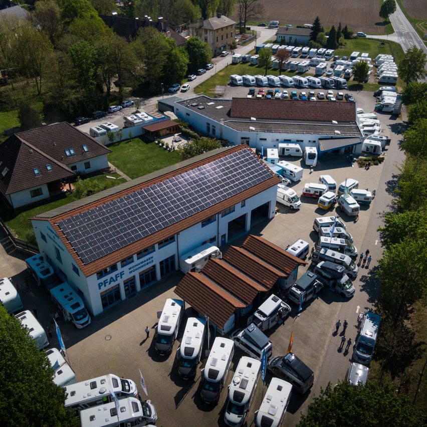 Luftaufnahme eines belebten Wohnmobil-Händlers mit Solarmodulen auf dem Dach und vielen Fahrzeugen auf dem Parkplatz.