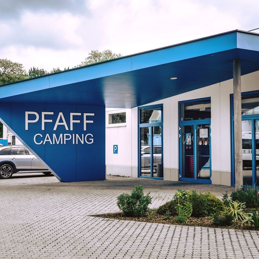 Ein blaues Gebäude mit dem Wort Pfaff Camping darauf. Ein silberner SUV ist auf der linken Seite des Gebäudes geparkt.