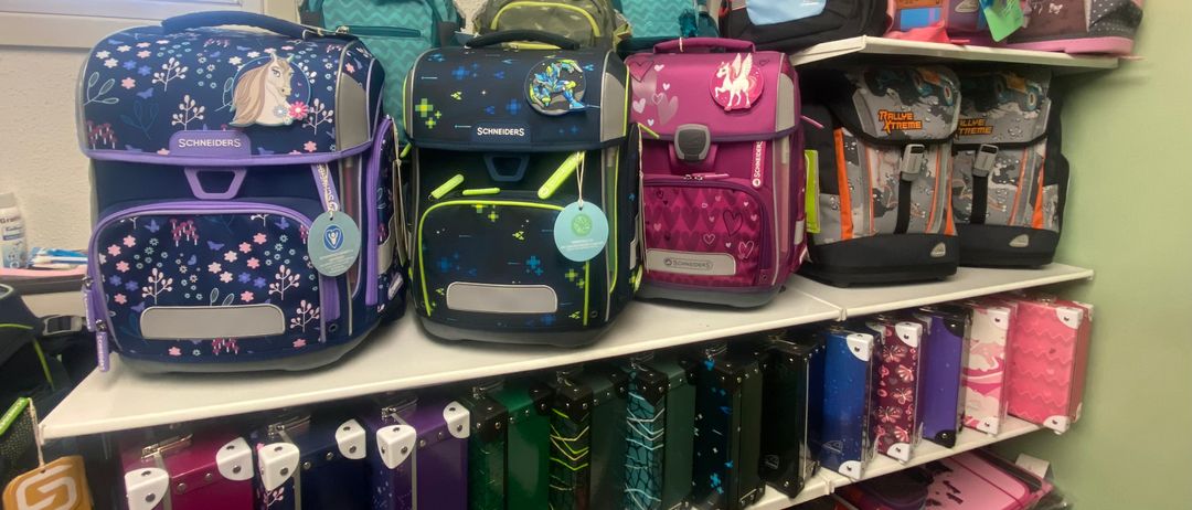 Ein Ladenregal gefüllt mit bunten Rucksäcken und Schulutensilien, darunter ein Pferde-Rucksack und ein Einhorn-Rucksack.