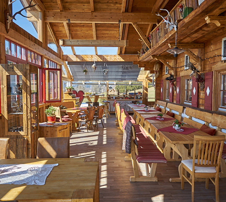 Ein hölzerner Innenraum eines Restaurants mit Holztischen und Stühlen, roten Fenstern und hölzernen Dekorationen.