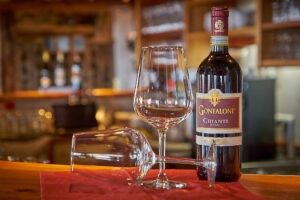 Eine Flasche Gonfaloni Wein steht auf einer Bartheke mit einem Weinglas und einem auf den Kopf gestellten Glas auf einem roten Tuch.