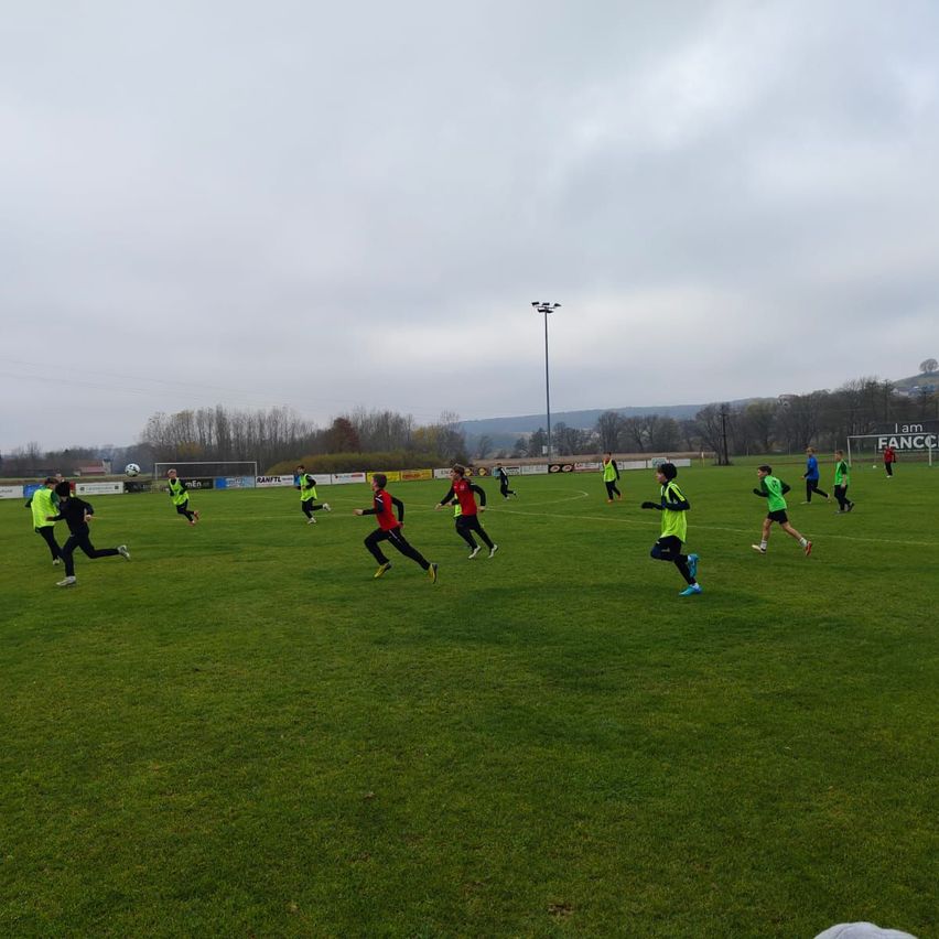 Eine Gruppe von Menschen in neongrünen und roten Trikots läuft auf einem Rasenfeld unter einem bewölkten Himmel.