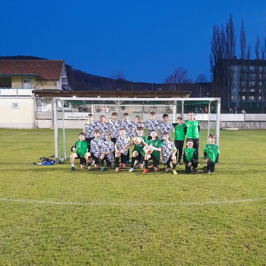 Eine Jugendfußballmannschaft in grünen und schwarzen Trikots posiert für ein Foto vor einem Tor bei klarem Nachthimmel.