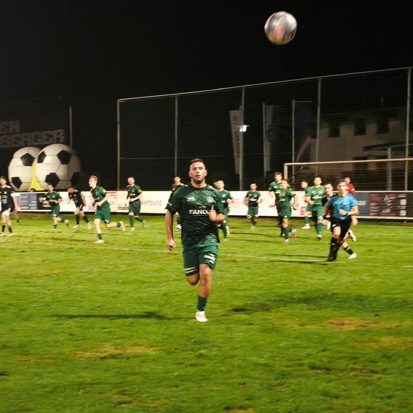 Ein Fußballspieler in einem grünen Trikot läuft in Richtung des Balls, der während eines Nachtspiels in der Luft fliegt.